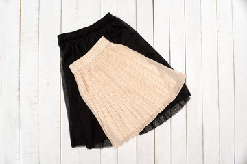 Black tulle and beige skirt on white wooden background. Top view