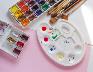 white plastic palette with a set of watercolor paints and brushes on a pink background, the artist's tools