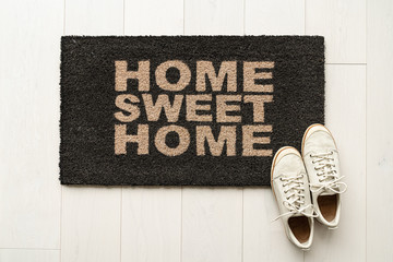 Home sweet home door mat at house entrance with women's sneakers of woman that has just arrived moved in. New condo. - obrazy, fototapety, plakaty