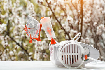 Nebulizer with a mask on the background of a blossoming tree. Spring exacerbation
