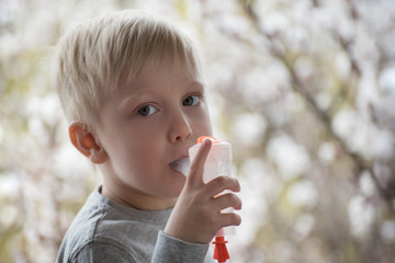 Blond boy makes inhalation at home. Flowering trees on backgdound. Prevention
