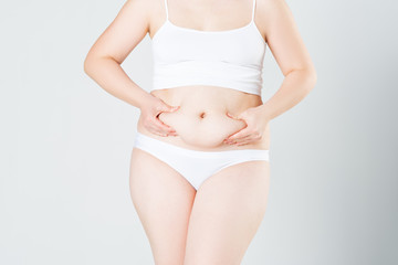 Woman holding fold of skin on thick belly, fat female body on gray background