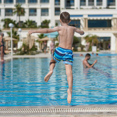 Naklejka premium European boy jumping into swimming pool at resort. Moment of taking off.