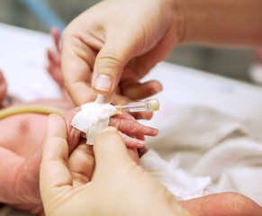 Nurse hands using medical adhesive plaster stick and wrap safely on IV Catheter and sick newborn baby's hand  for prepare fill the saline solution and medicine.