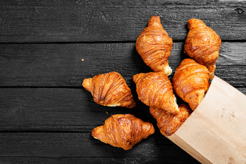 Freshly baked croissants on black wooden table, top view.