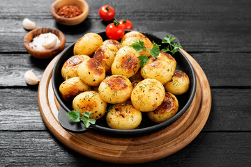 Roasted new potato in frying pan on black wooden background.