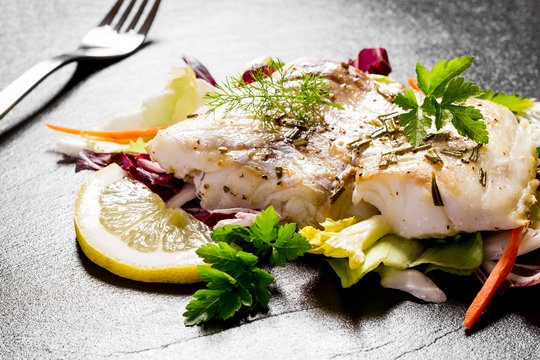 Grilled cod fillet with salad on black slate plate
