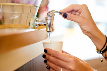 Close up of female hands filling pepper cup with fresh water from the cooler,