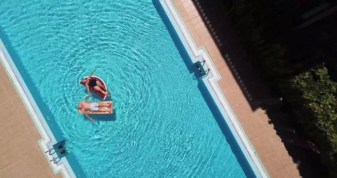 Top vertical view of swimming pool in hotel residence vacation with people adult senior lay down and enjoy with inflatables lilos mattress on blue water - alternative lifestyle for summer vibes