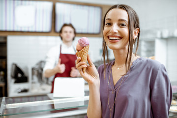 Portrait of a young and happpy woman buying ice cream in the pastry shop with salesman on the background