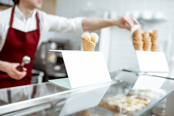 Ice cream in the waffle cone on the counter of the pastry shop with salesperson on the background