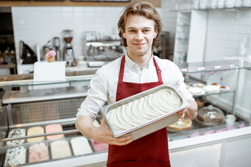 Portrait of a handsome salesman or confectioner in red apron holding tray with ice cream in the shop