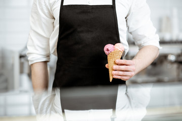 Salesman holding ice cream in the waffle cone on the black apron background in the shop, close-up...