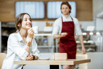 Handsome waiter in red apron serving sweet cake for a young woman customer at the pastry shop or cafe