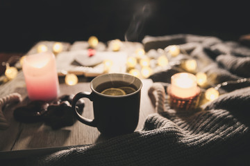 Obraz na płótnie Canvas Holidays mood photo. Christmas lights and warm knitted sweater. Hot tea mug with a book for cosy evening. Sweet gingerbread and wooden heart on tray. Perfect winter flat lay with candle. Hygge concept