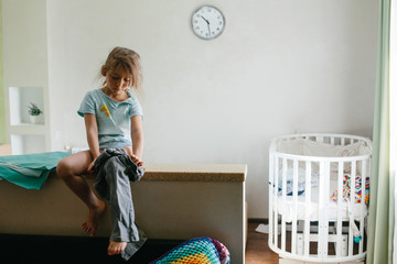 Little girl kid getting dressed by herself, going to kindergarten in the morning. Clock on the wall in bedroom