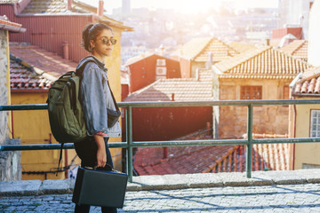 Young woman wearing sunglasses, backpack and black suitcase travel and walking in European old city...