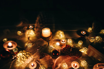 Candles burning among beautiful Christmas lights and garland decorations. New Year festive background. Presents, gifts, greeting postcard for winter holidays.