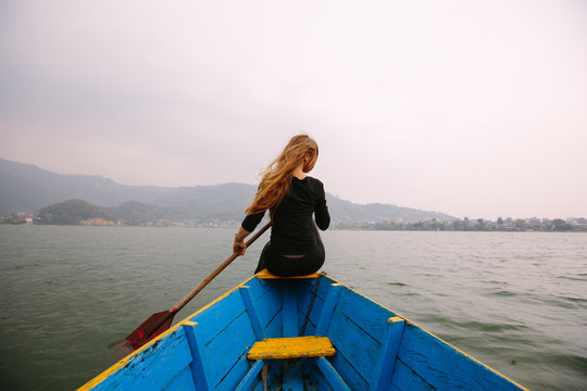 Woman in black clothes sitting on boat with paddle, nice mountain lake Fewa on background