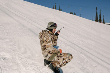 Man snowboarder using walkie talkie on slope. Ski resort emergency