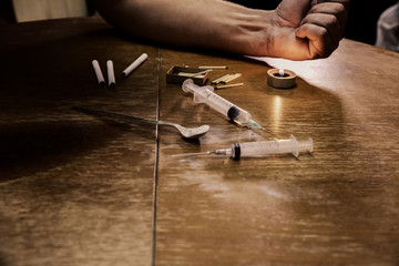 Man's hand near needle syringe lying on the table. Drugs addict. Candle burning with matches and cigarettes. Heroin in the spoon. Dangerous habit. Unhealthy life concept.
