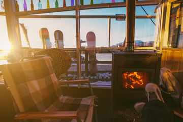 Snowboarder legs near fireplace in Ski resort caffe on sunset