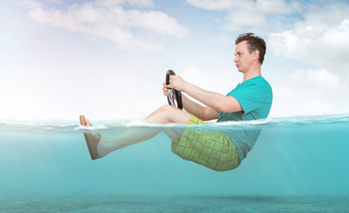 Funny man in shorts, T-shirt and sandals rides on the sea with a car steering wheel. Concept of going on vacation