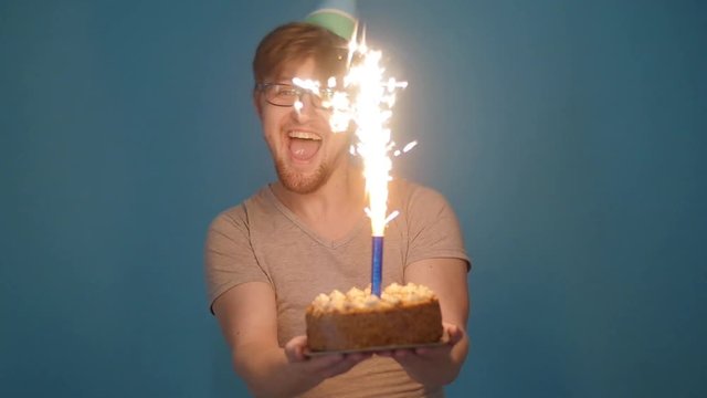 Concept of celebration and fun. Smiling happy crazy young man in party hat holding a birthday cake
