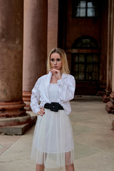Fashion look's woman. Young woman modern portrait. Young woman dressed in white skirt and shirt posing near the old looking soviet union's architectural building with large pillars and bas-reliefs.