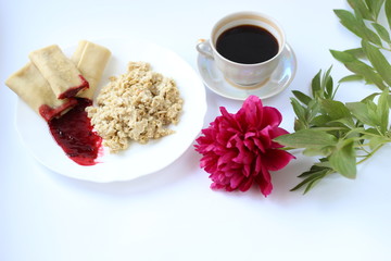 breakfast of oatmeal and pancakes with berries and a cup of coffee and next to a peony flower