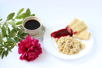 breakfast of oatmeal and pancakes with berries and a cup of coffee and next to a peony flower