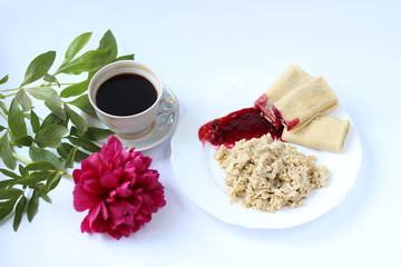 breakfast of oatmeal and pancakes with berries and a cup of coffee and next to a peony flower