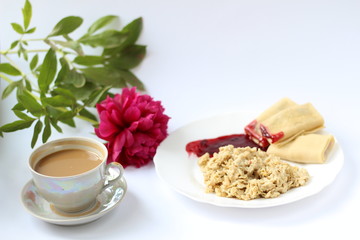 breakfast of oatmeal and pancakes with berries and a cup of coffee and next to a peony flower