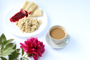 breakfast of oatmeal and pancakes with berries and a cup of coffee and next to a peony flower