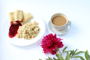 breakfast of oatmeal and pancakes with berries and a cup of coffee and next to a peony flower