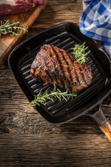 Grilled beef steak in grill pan with herbs rosemary on wooden table