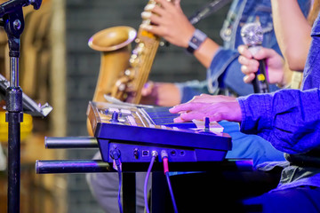 Closeup and crop group of musician playing an electronic keyboard, saxophone and singing on stage with blue lighting on blurry background.
