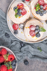 Mini pavlova meringue cakes with fresh raspberries and blueberries with mint leaves.