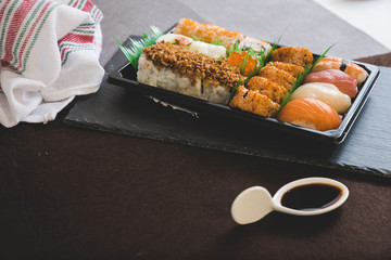 Eating sushi. Japanese food restaurant, unagi and salmon sushi on dark background. Taking piece with chopsticks. Closeup on black wood