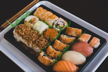 Eating sushi. Japanese food restaurant, unagi and salmon sushi on dark background. Taking piece with chopsticks. Closeup on black wood
