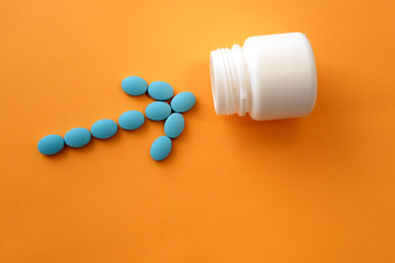 The tablets form an arrow pointing to an empty jar . Symbolic image. A bunch of blue pills on an orange background. The concept of pharmacology. The correct treatment concept.