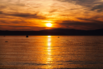 Fototapeta premium Orange sunset on the sea with the sun, a beautiful sky on the background of mountains