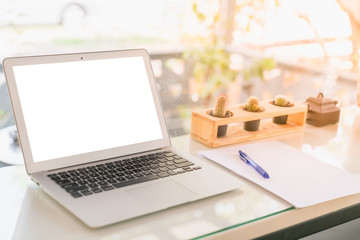 Laptop with white blank screen to insert picture or text and a pen with white paper on table at cafe with cactus and orange sunlight