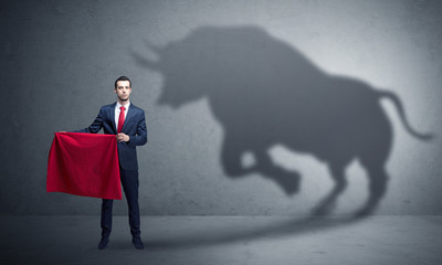 Businessman standing with red cloth in his hand and big bull shadow on the wall
