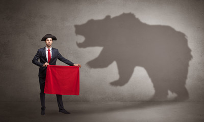 Businessman standing with red cloth in his hand and big bear shadow on his background
