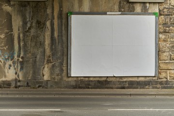White blank billboard at the wall of an old railroad underpass.