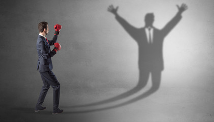 Businessman with boxing gloves fighting with disarmed businessman shadow

