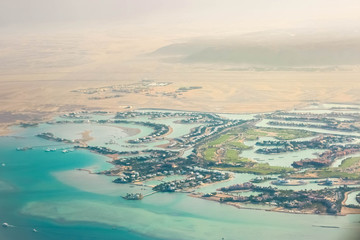 View from a plane window on the resort beach area of the Red Sea. It is visible a part of the desert, lodges of hotels, greens oases, blue coastal transparent water, coral reeves