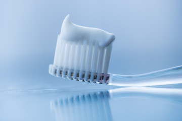 Fototapeta na wymiar Transparent plastic toothbrush with white toothpaste on a blue white background with reflection on the glass.
