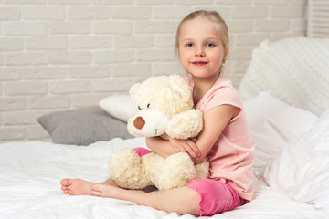 adorable little child girl hugging teddy bear in bed in morning.